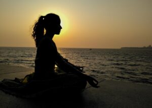 Healing as resistance and why your wellness matters. Picture of a woman against the sunset meditating