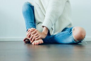 Woman seated with jeans and white shirt holding her feet